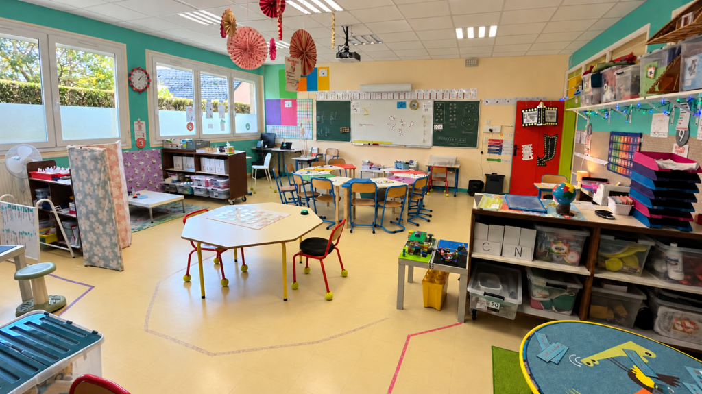Classe flexible au CP avec tables de travail en petits groupes, assises variées et espaces délimités par des repères colorés au sol.